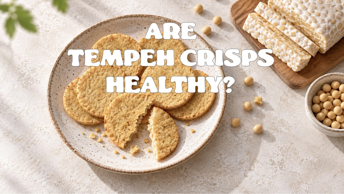 round baked tempeh crisps on a speckled ceramic plate, one broken in half, with a block of fresh tempeh and a bowl of soya beans alongside.