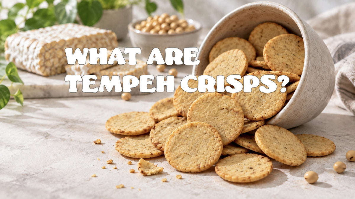 round baked tempeh crisps spilling from a stoneware pot beside a block of fresh tempeh and a bowl of soya beans.